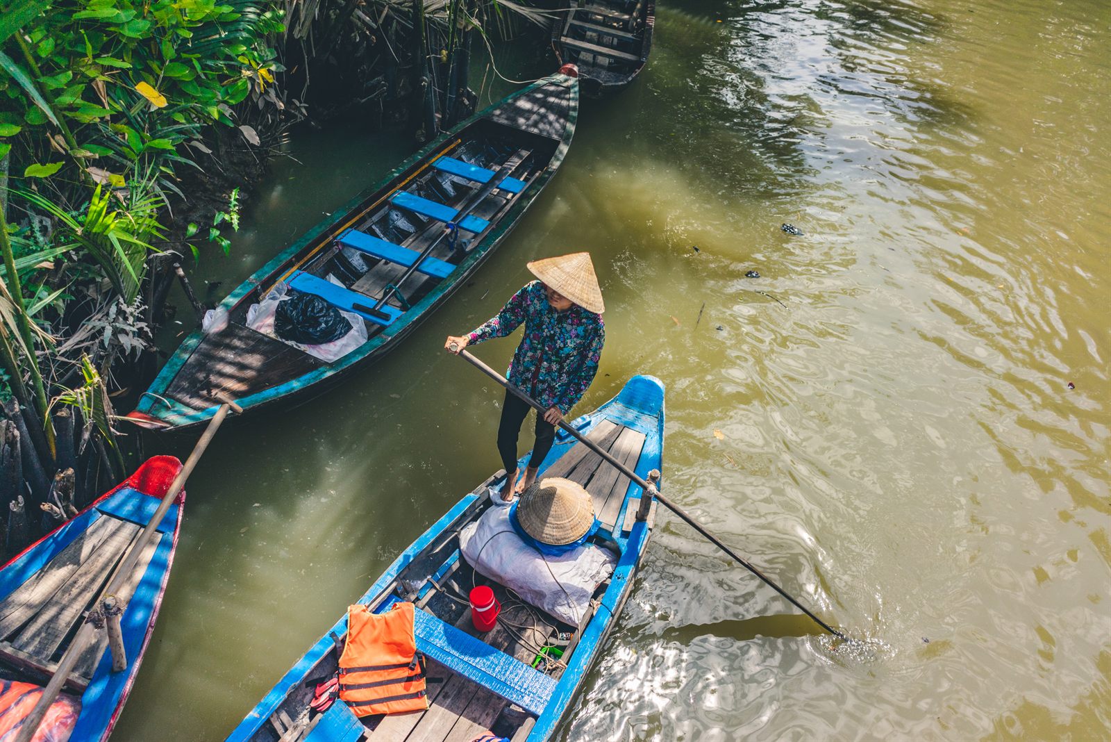 Woman in a conical hat poling a wooden boat on a Mekong Delta canal in Vietnam, a classic sight on Asia river cruises